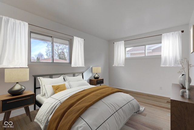 bedroom with multiple windows, baseboards, and wood finished floors