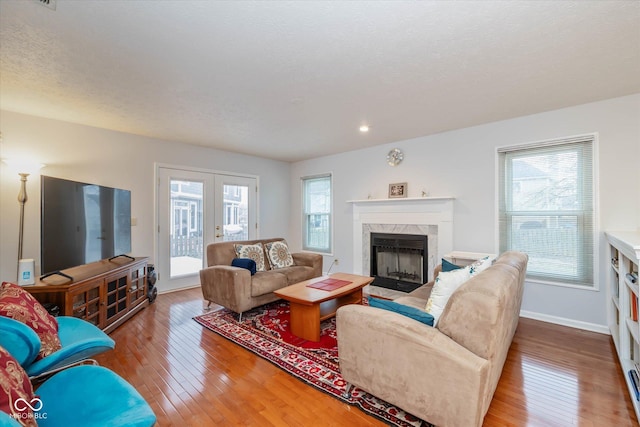 living room featuring a high end fireplace, light hardwood / wood-style floors, french doors, and a textured ceiling