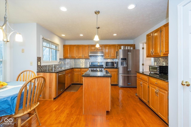 kitchen with appliances with stainless steel finishes, a center island, hardwood / wood-style floors, and decorative light fixtures