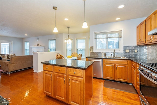 kitchen featuring appliances with stainless steel finishes, decorative light fixtures, sink, decorative backsplash, and a center island