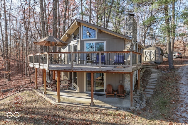 rear view of house featuring a wooden deck, a shed, and a patio