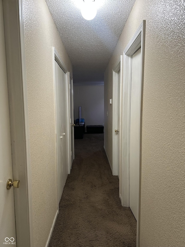 hall featuring a textured ceiling and dark colored carpet