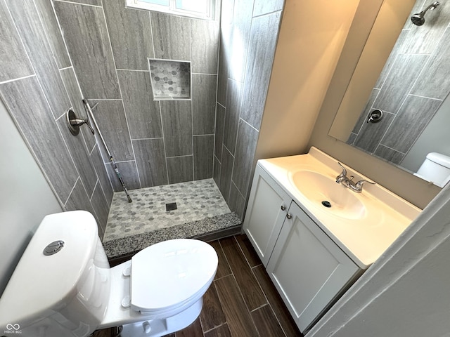 full bath featuring vanity, wood finish floors, a tile shower, and toilet