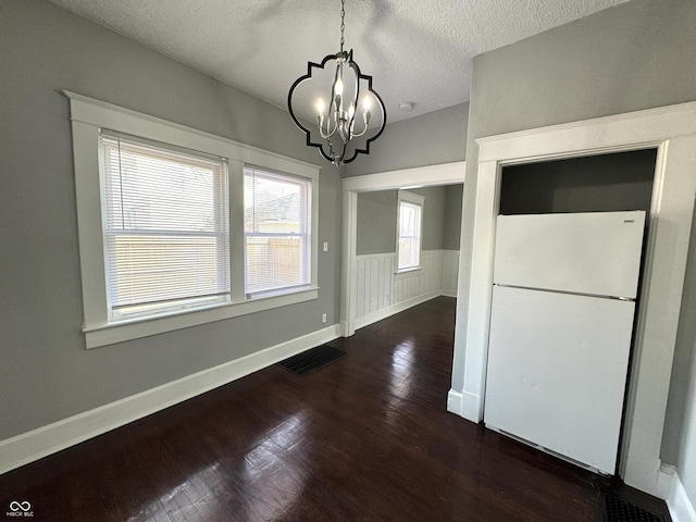 unfurnished dining area with a wainscoted wall, visible vents, an inviting chandelier, a textured ceiling, and wood finished floors