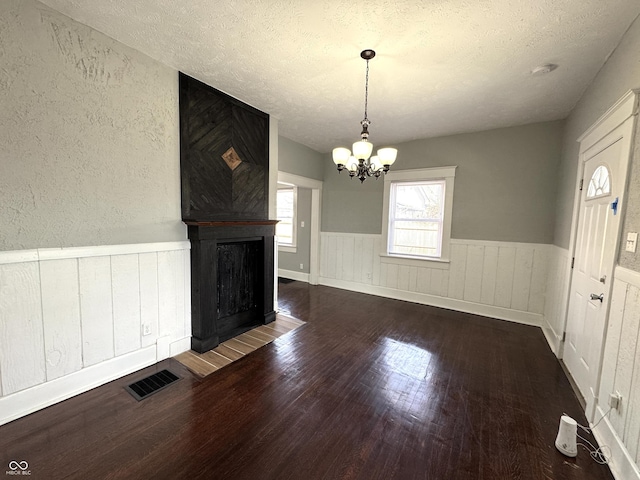 unfurnished living room featuring visible vents, wainscoting, a textured ceiling, wood finished floors, and a chandelier