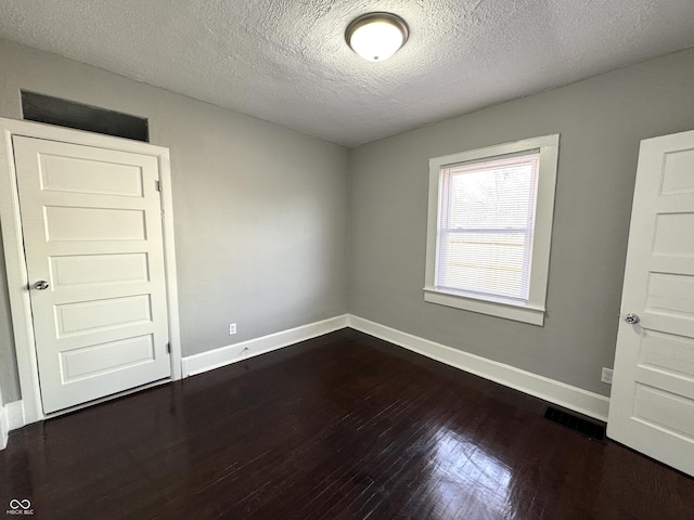 unfurnished room with dark wood-type flooring, visible vents, a textured ceiling, and baseboards