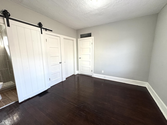 unfurnished bedroom with a barn door, dark wood finished floors, visible vents, and baseboards