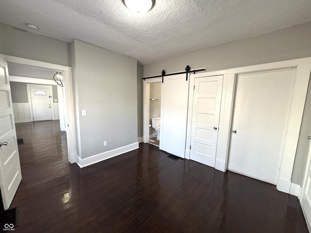 unfurnished bedroom with a textured ceiling, ensuite bathroom, a barn door, wood finished floors, and baseboards