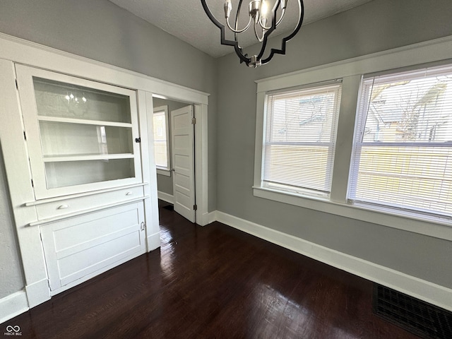 unfurnished dining area featuring dark wood finished floors, a notable chandelier, visible vents, a textured ceiling, and baseboards