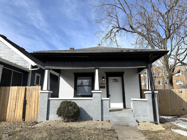 bungalow featuring a porch, fence, and brick siding