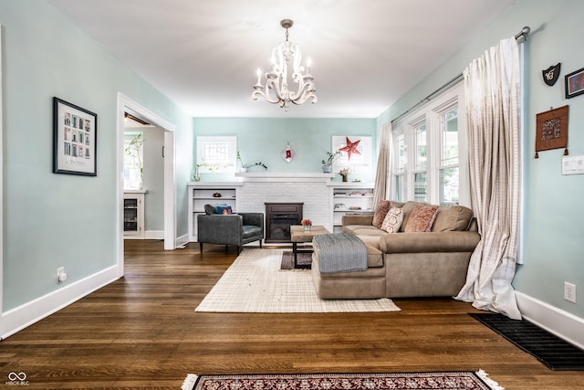 living room with a brick fireplace, a notable chandelier, and dark wood-type flooring