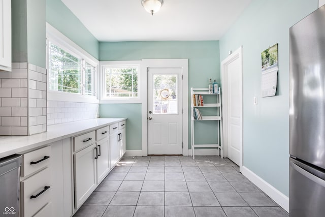 kitchen featuring light tile patterned floors, appliances with stainless steel finishes, white cabinetry, light stone countertops, and decorative backsplash