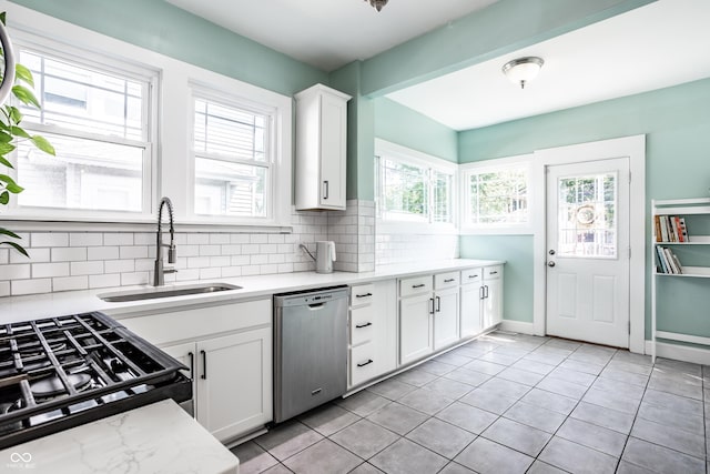 kitchen with light tile patterned flooring, tasteful backsplash, white cabinetry, dishwasher, and sink