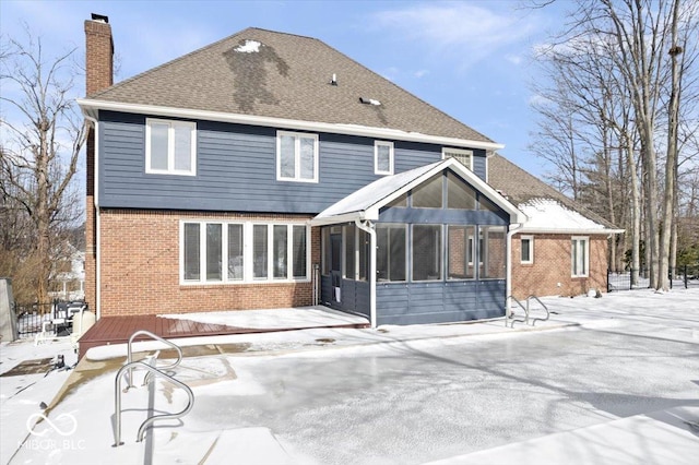 snow covered back of property featuring a sunroom