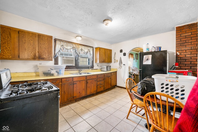 kitchen with light tile patterned flooring, sink, gas stove, a textured ceiling, and stainless steel refrigerator