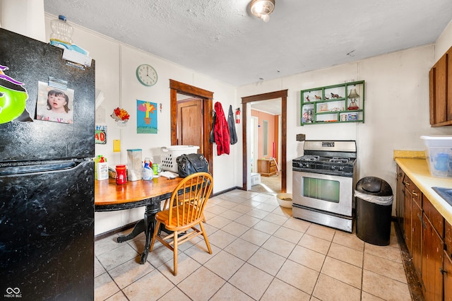 kitchen with black refrigerator, light tile patterned flooring, a textured ceiling, and stainless steel gas stove