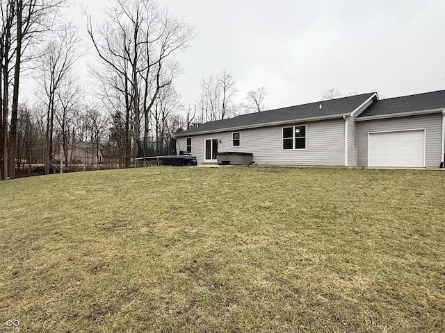 rear view of house with a hot tub, a garage, a yard, and a trampoline