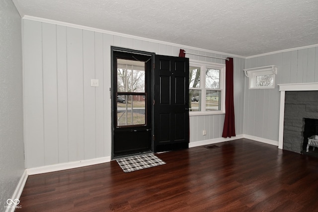 entryway with dark wood-type flooring, a stone fireplace, a textured ceiling, and crown molding