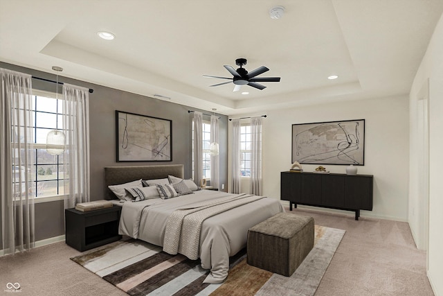 bedroom featuring a raised ceiling, light carpet, and multiple windows