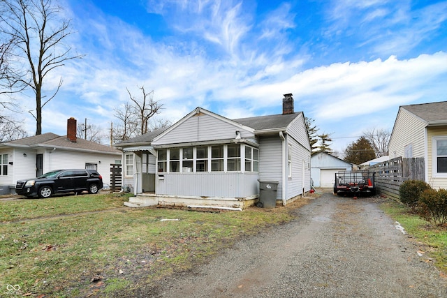 bungalow-style home with an outbuilding, a garage, a front lawn, and a sunroom