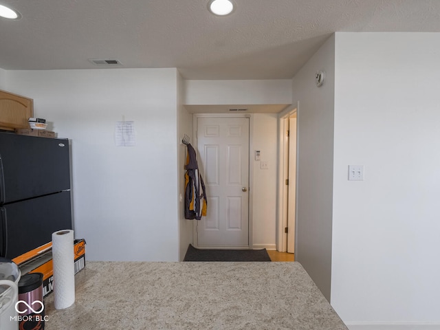 kitchen with black refrigerator, light brown cabinetry, and a textured ceiling