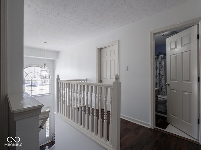 hallway with dark wood-type flooring, a chandelier, and a textured ceiling