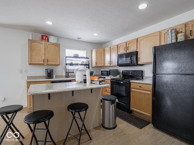 kitchen with light hardwood / wood-style flooring, a kitchen breakfast bar, a center island, black appliances, and light brown cabinetry