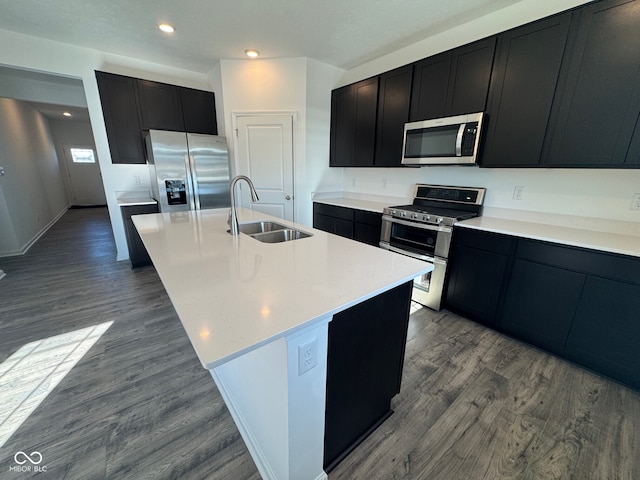 kitchen with wood-type flooring, appliances with stainless steel finishes, sink, and a center island with sink