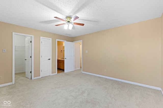 unfurnished bedroom featuring ensuite bathroom, a textured ceiling, light carpet, a spacious closet, and a closet