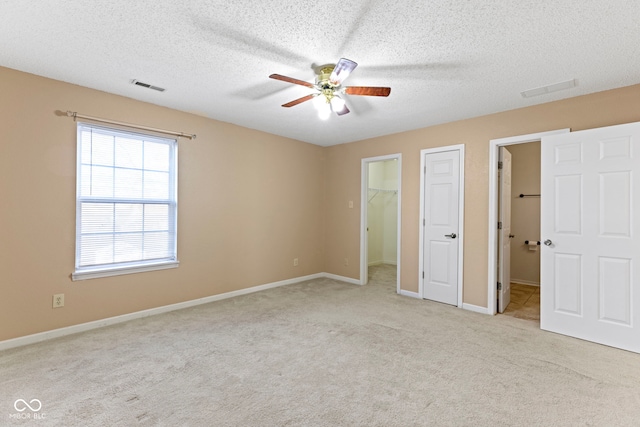 unfurnished bedroom with ceiling fan, a textured ceiling, light carpet, a spacious closet, and a closet