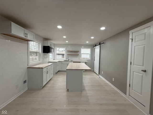 kitchen with sink, white cabinets, a center island, a barn door, and light wood-type flooring