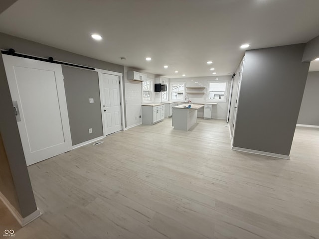 unfurnished living room featuring a wall mounted air conditioner, light hardwood / wood-style floors, and a barn door