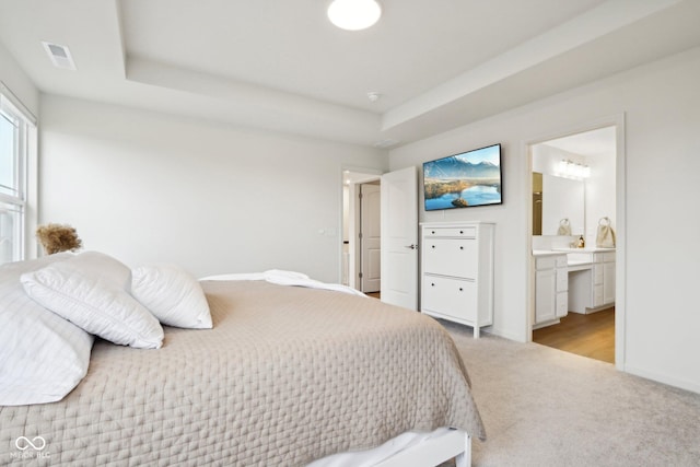 carpeted bedroom with ensuite bath and a raised ceiling