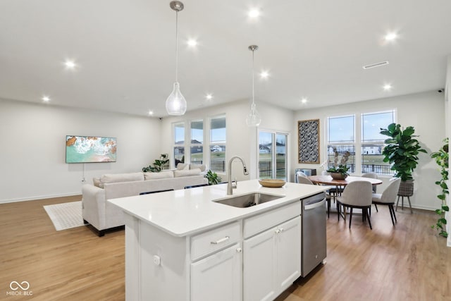 kitchen with sink, stainless steel dishwasher, pendant lighting, a kitchen island with sink, and white cabinets