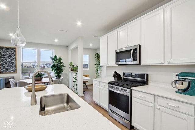 kitchen with pendant lighting, sink, appliances with stainless steel finishes, light stone counters, and white cabinets