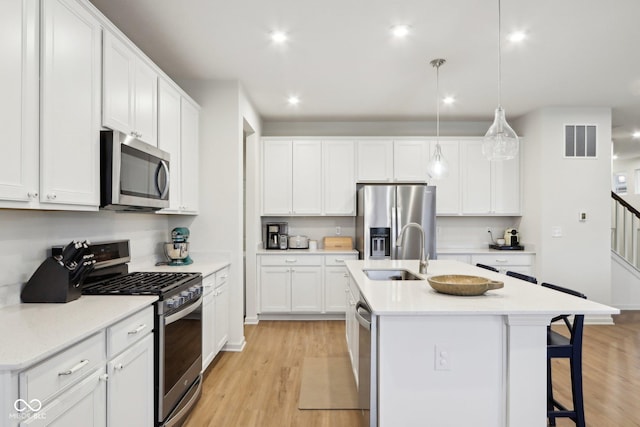 kitchen with decorative light fixtures, sink, white cabinets, stainless steel appliances, and a center island with sink