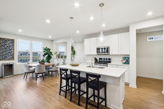 kitchen featuring stainless steel appliances, pendant lighting, a center island with sink, and white cabinets