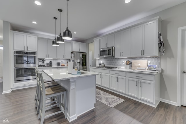 kitchen featuring a breakfast bar, an island with sink, hanging light fixtures, stainless steel appliances, and light stone countertops