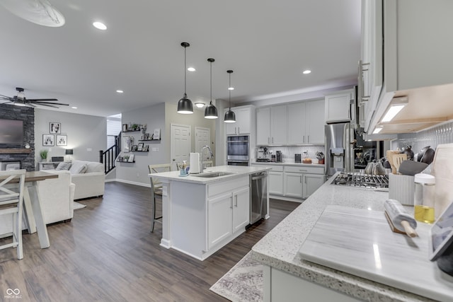 kitchen featuring a kitchen island with sink, sink, light stone countertops, and hanging light fixtures