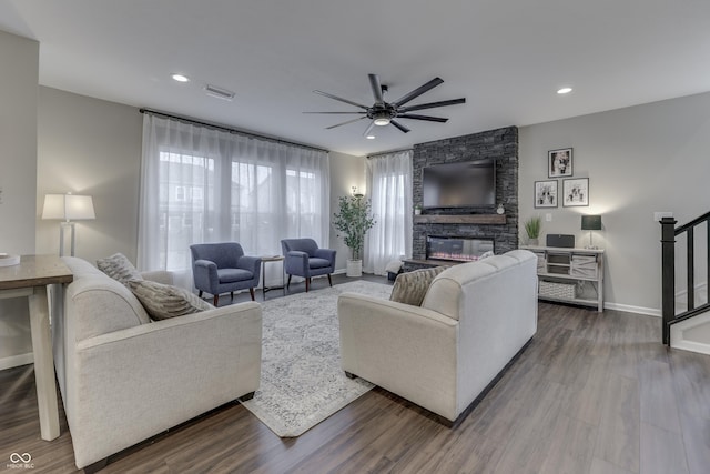 living room with wood-type flooring, a stone fireplace, and ceiling fan