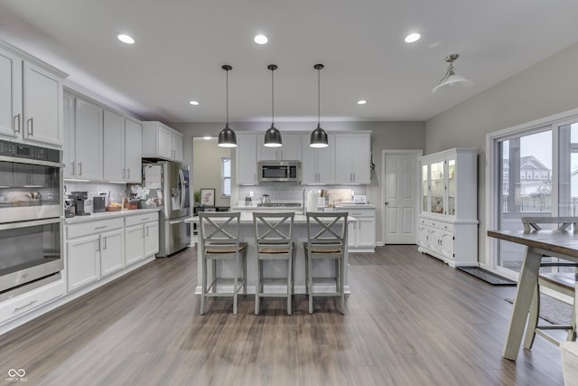 kitchen with appliances with stainless steel finishes, decorative light fixtures, white cabinetry, an island with sink, and a kitchen bar