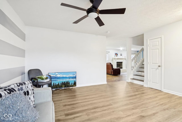 living area featuring ceiling fan, a fireplace, and light hardwood / wood-style flooring