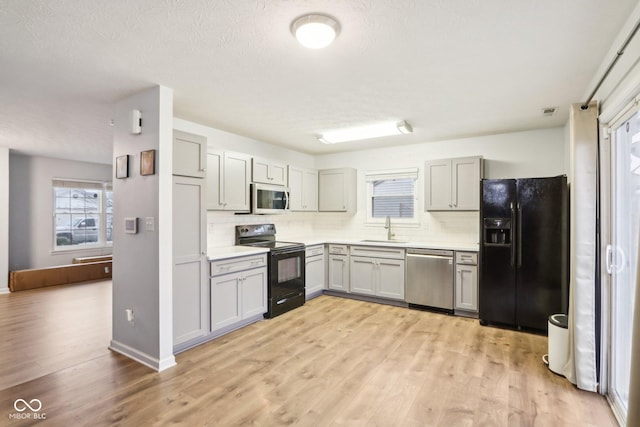 kitchen with light hardwood / wood-style floors, gray cabinets, sink, and black appliances