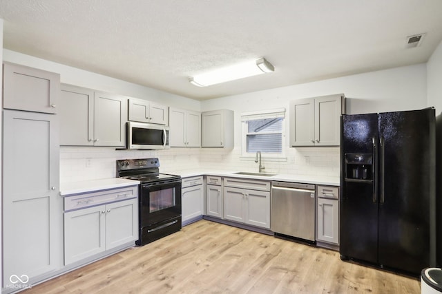 kitchen with sink, gray cabinetry, backsplash, light hardwood / wood-style floors, and black appliances