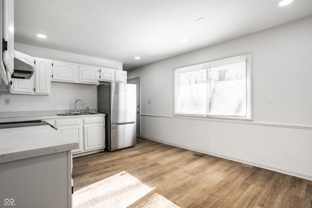 kitchen featuring stainless steel refrigerator, ventilation hood, white cabinetry, sink, and light hardwood / wood-style floors