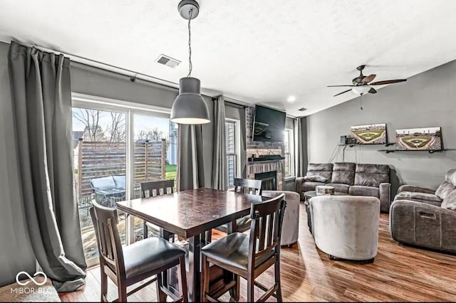 dining area with vaulted ceiling, a brick fireplace, wood-type flooring, and ceiling fan