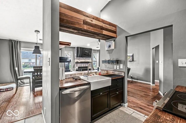 kitchen featuring a stone fireplace, dishwasher, sink, hanging light fixtures, and ceiling fan