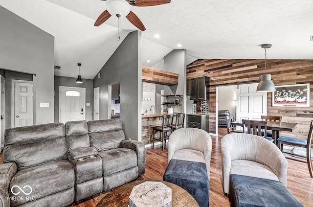 living room with ceiling fan, wooden walls, high vaulted ceiling, light hardwood / wood-style floors, and a barn door