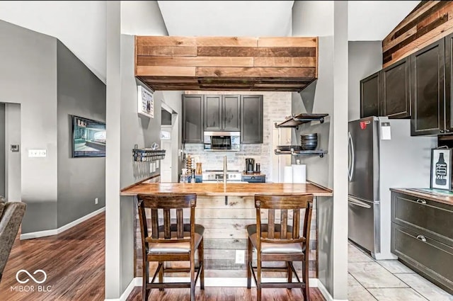 kitchen with wood counters, dark brown cabinets, tasteful backsplash, and appliances with stainless steel finishes