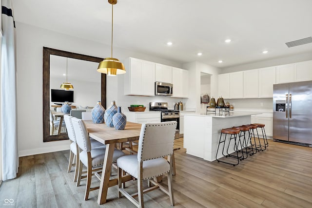 kitchen with a kitchen island, appliances with stainless steel finishes, decorative light fixtures, white cabinets, and light wood-type flooring